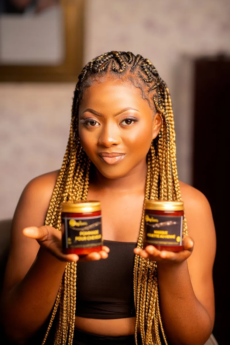 Cliente aux tresses dorées présentant deux pots de pommade capillaire Das'hair